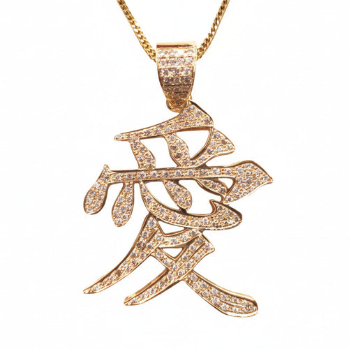 A gold pendant necklace featuring a stylized Chinese calligraphy character for 'Love' (爱), embellished with small clear pavé stones, suspended from a gold chain against a plain white background.